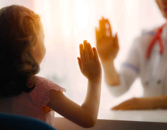 Child and healthcare professional giving a high-five across a table in a bright setting.